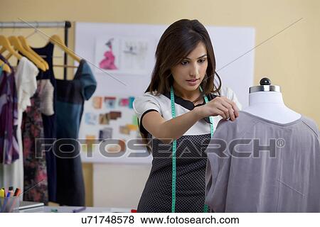 Stock Photo - Young female fashion designer working on garment on dressmaker's model . Fotosearch