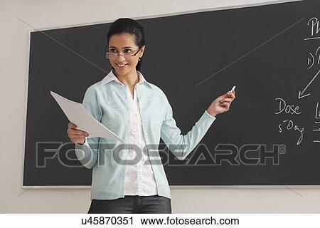 Young female lecturer holding papers and chalk against blackboard View Large Photo Image Stock Image - Young female lecturer holding papers and chalk against blackboard . Fotosearch
