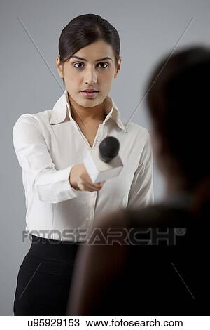Stock Image - Young female reporter taking interview of a person . Fotosearch