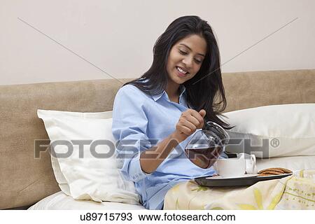 Young female smiling while having morning tea and breakfast in bed View Large Photo Image Stock Image - Young female smiling while having morning tea and breakfast in bed . Fotosearch