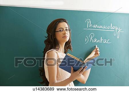 Young female teacher explaining a lesson while standing against green board View Large Photo Image Stock Photo - Young female teacher explaining a lesson while standing against green board . Fotosearch