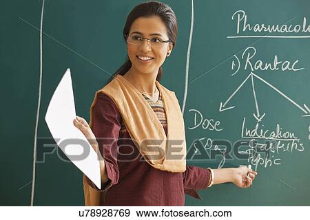 Young female teacher explaining a lesson while standing against chalkboard View Large Photo Image Stock Photo - Young female teacher explaining a lesson while standing against chalkboard . Fotosearch
