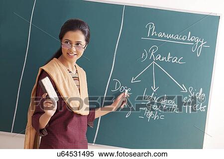 Stock Photography - Young female teacher explaining a lesson while holding chalk and duster against green board . Fotosearch