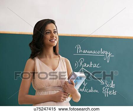 Young female teacher holding books while looking away against green board View Large Photo Image Stock Photography - Young female teacher holding books while looking away against green board . Fotosearch