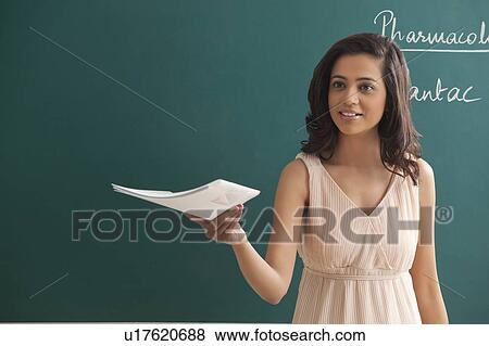 Young female teacher holding file while looking away against green board View Large Photo Image Stock Photo - Young female teacher holding file while looking away against green board . Fotosearch
