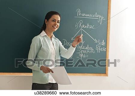 Young female teacher holding paper and chalk against green board View Large Photo Image Stock Image - Young female teacher holding paper and chalk against green board . Fotosearch