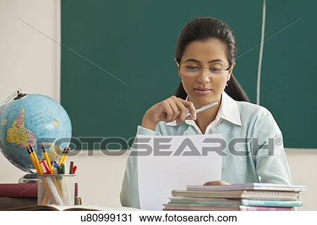 Stock Image - Young female teacher reading document at desk . Fotosearch