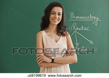 Young female teacher standing with arms crossed against green board View Large Photo Image Stock Photo - Young female teacher standing with arms crossed against green board . Fotosearch
