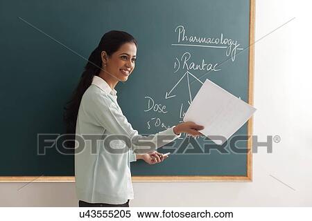 Young female teacher with papers explaining by chalkboard View Large Photo Image Stock Photography - Young female teacher with papers explaining by chalkboard . Fotosearch