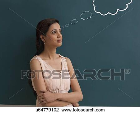 Stock Image - Young female teacher with thought bubble on chalk board . Fotosearch
