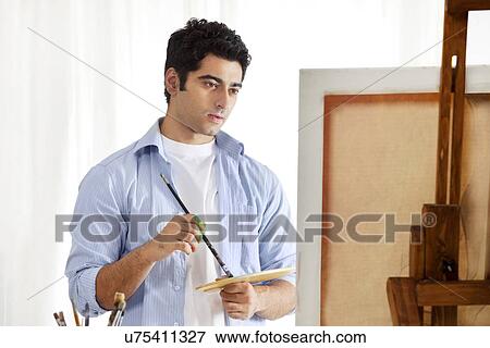 Stock Photo - Young handsome man holding palette and paintbrush while painting . Fotosearch