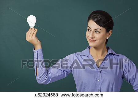 Stock Photo - Young Indian businesswoman holding light bulb against green board at office. Fotosearch