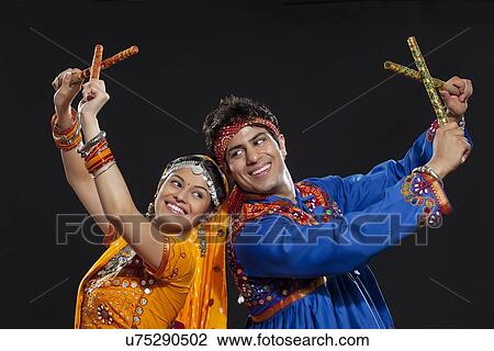Young Indian couple in traditional wear performing Dandiya Raas against black background View Large Photo Image Stock Image - Young Indian couple in traditional wear performing Dandiya Raas against black background. Fotosearch