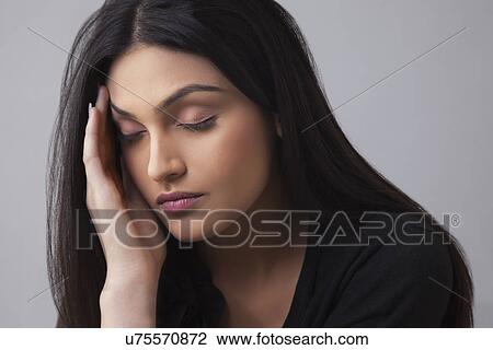 Stock Image - Young Indian female suffering from headache over colored background . Fotosearch