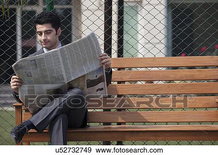 Young male business corporate executive reading newspaper while sitting on bench in tennis court View Large Photo Image Stock Photo - Young male business corporate executive reading newspaper while sitting on bench in tennis court . Fotosearch