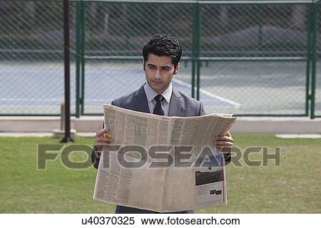 Young male executive reading newspaper in a tennis court View Large Photo Image Stock Photography - Young male executive reading newspaper in a tennis court . Fotosearch