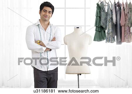 Stock Image - Young male fashion designer standing by mannequin in studio . Fotosearch