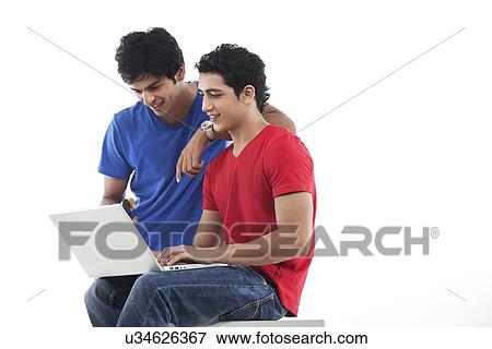Stock Photo - Young male friends looking at laptop over white background . Fotosearch