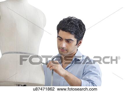 Stock Image - Young male tailor measuring waist of mannequin . Fotosearch
