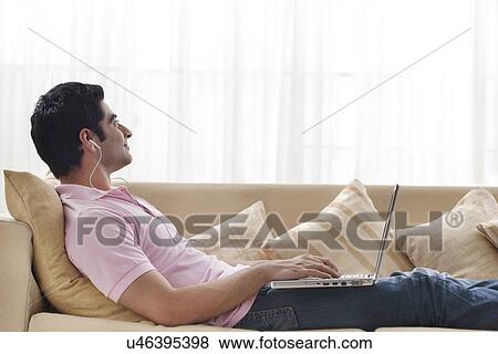 Stock Photo - Young man contemplating while listening to music with laptop . Fotosearch