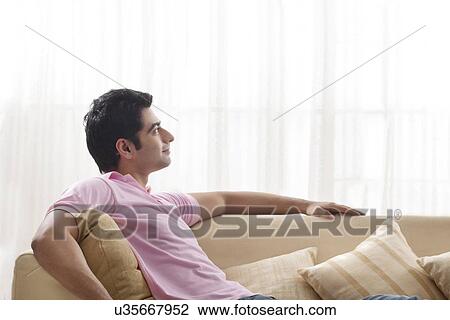 Stock Image - Young man day dreaming while relaxing on sofa . Fotosearch