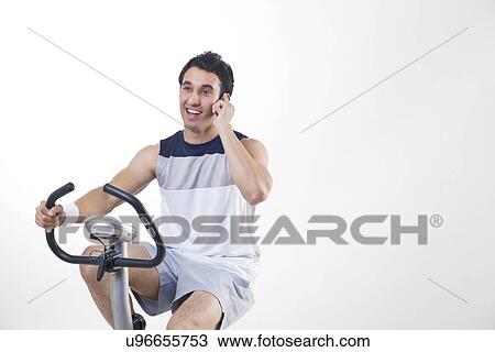 Young man exercising while talking on cell phone over white background View Large Photo Image Stock Image - Young man exercising while talking on cell phone over white background . Fotosearch
