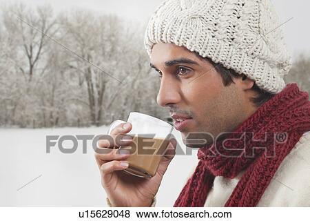 Stock Photo - Young man in warm clothes drinking tea . Fotosearch