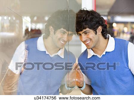 Stock Photograph - Young man looking at his reflection . Fotosearch