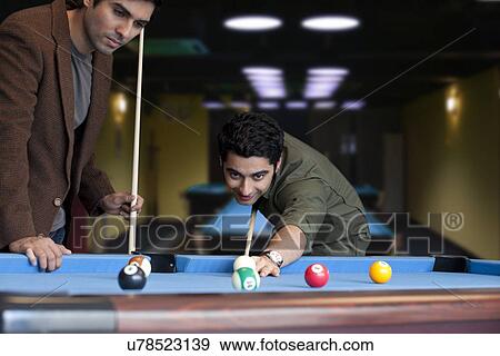 Stock Photo - Young man playing snooker while friend standing besides . Fotosearch