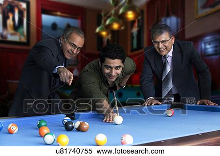 Stock Photography - Young man playing snooker while senior businessmen standing by pool table . Fotosearch