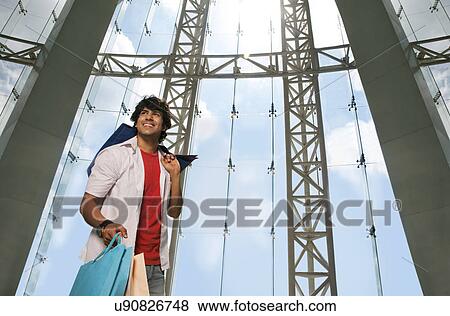 Stock Photo - Young man smiling while holding shopping bags . Fotosearch
