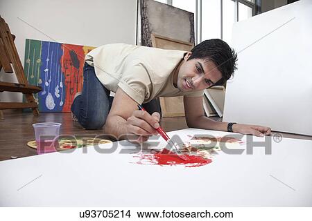 Picture - Young man smiling while painting on a large canvas at an art studio . Fotosearch