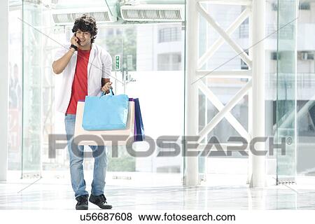 Young man speaking on phone with shopping bags View Large Photo Image Stock Photo - Young man speaking on phone with shopping bags . Fotosearch