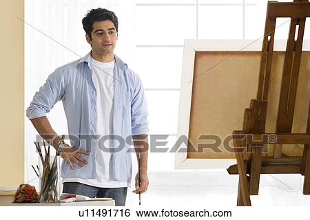 Young man standing in front of easel View Large Photo Image Stock Photograph - Young man standing in front of easel . Fotosearch