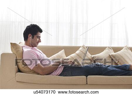 Stock Image - Young man using laptop while listening to music . Fotosearch