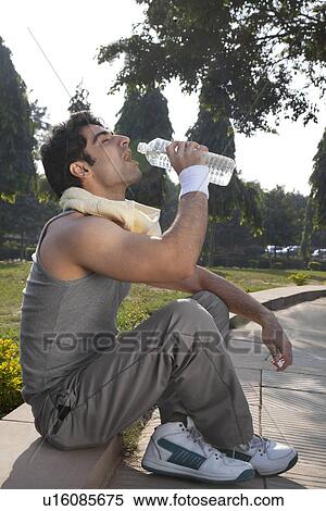Stock Photography - Young man with towel round shoulders drinking water after sport activities . Fotosearch