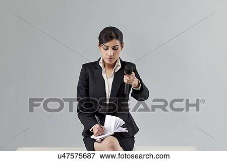 Young news reporter holding out microphone while writing in notepad View Large Photo Image Stock Photo - Young news reporter holding out microphone while writing in notepad . Fotosearch