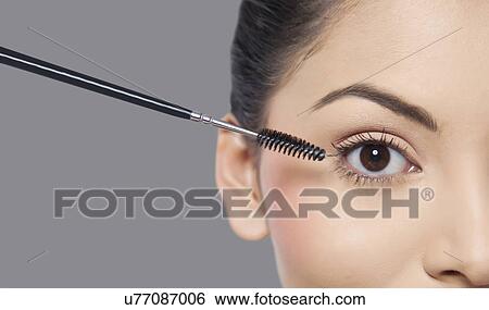 Stock Photograph - Young woman applying mascara over grey background . Fotosearch