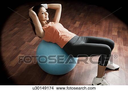 Picture - Young woman balancing on exercise ball with hands behind head . Fotosearch