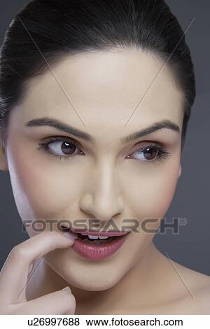 Young woman biting fingernail while looking away over colored background View Large Photo Image Stock Photo - Young woman biting fingernail while looking away over colored background . Fotosearch