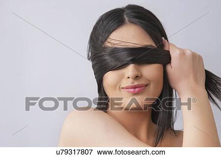Stock Photo - Young woman covering eyes with her hair over colored background . Fotosearch