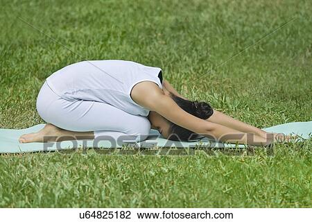 Stock Image - Young woman doing yoga on a lawn . Fotosearch