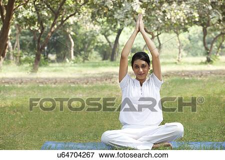 Stock Photo - Young woman doing yoga with arms raised . Fotosearch