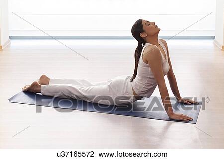 Stock Image - Young woman doing yogic 'sun salutation' on mat. Fotosearch
