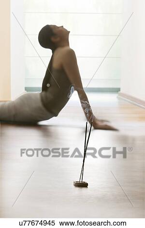 Stock Photography - Young woman doing yogic 'sun salutation' on floor with incense sticks in the foreground. Fotosearch