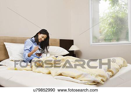 Young woman having her morning tea in bed View Large Photo Image Stock Image - Young woman having her morning tea in bed . Fotosearch