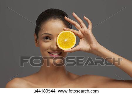 Young woman holding an orange slice over her eye View Large Photo Image Picture - Young woman holding an orange slice over her eye . Fotosearch