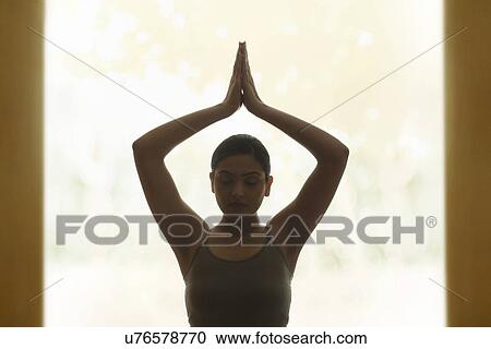 Stock Image - Young woman holding hands up in yoga pose. Fotosearch