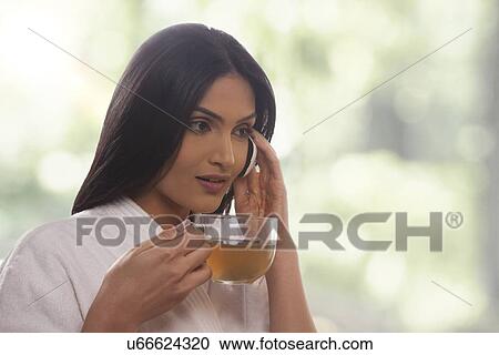 Young woman holding tea cup while on call View Large Photo Image Stock Image - Young woman holding tea cup while on call . Fotosearch
