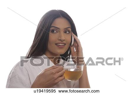Stock Photography - Young woman holding tea cup while using cell phone . Fotosearch